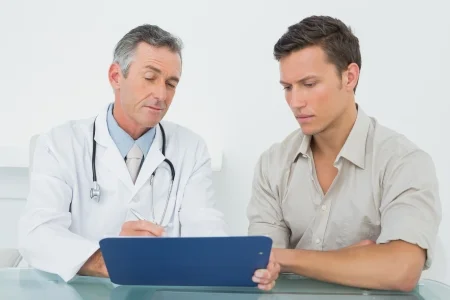 25459439 male doctor discussing reports with patient at desk in medical office