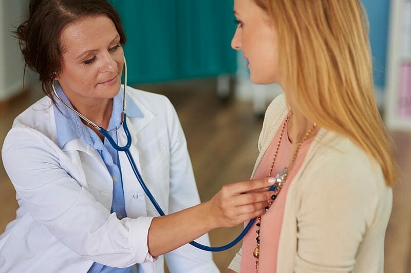 female doctor checking womans heartbeat with a stethoscope