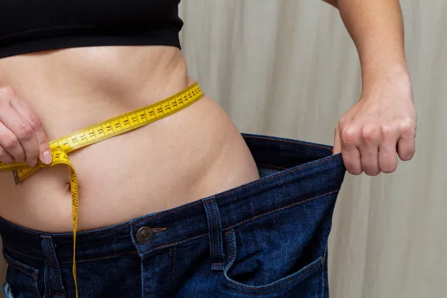 slim woman holding very big jeans after weight-loss